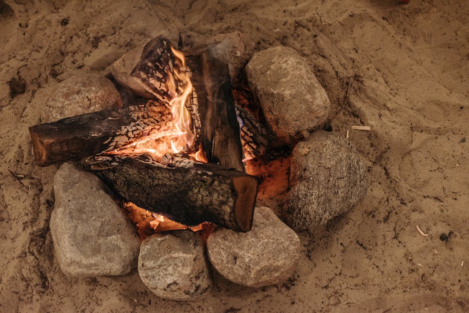 Warm campfire burning in sand surrounded by rocks, perfect for outdoor adventures.