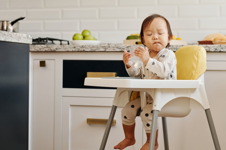 Cute toddler in polka dot pajamas drinking from a glass in a stylish kitchen.