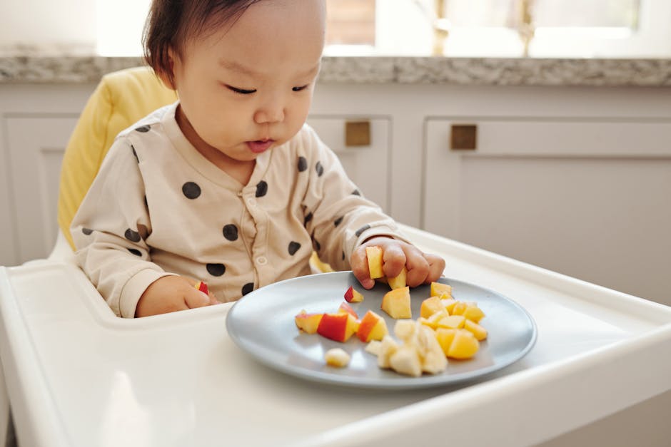 Adorable baby enjoying fresh fruit slices in a modern kitchen setting.
