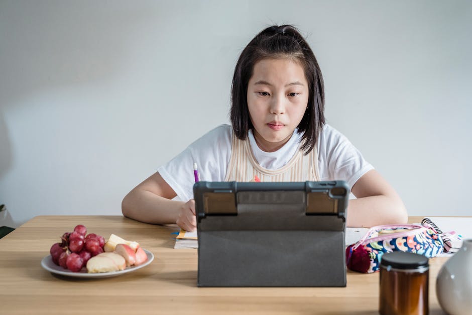 Young girl studies on a tablet with snacks on the table, blending learning and leisure.