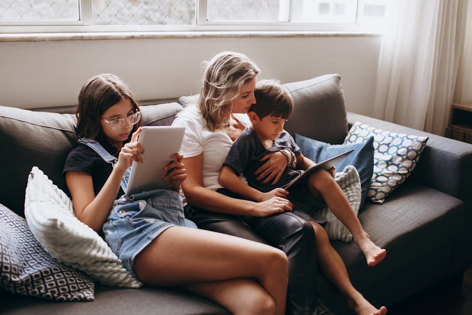 Mother and two children using tablets on the sofa, enjoying a quiet family moment indoors.