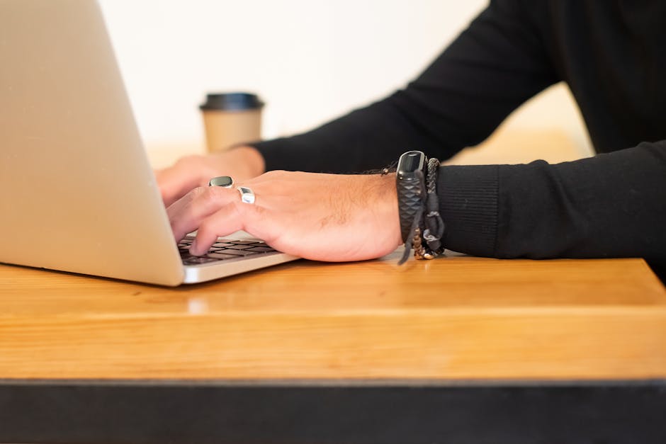 Close-up of hands typing on a laptop with a coffee cup in the background, highlighting modern work lifestyle.