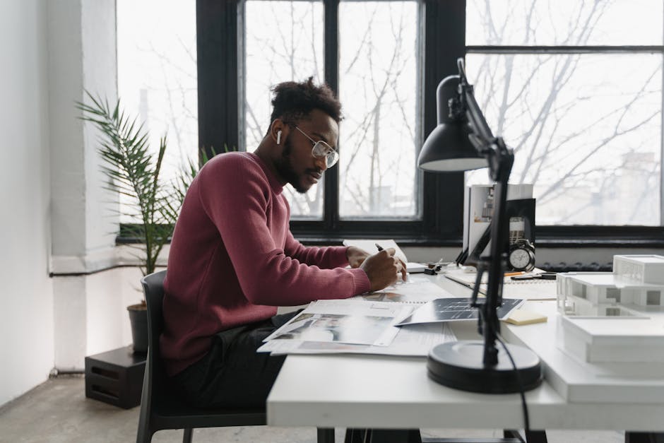 Architect focused on designing at desk with natural window light in modern office.