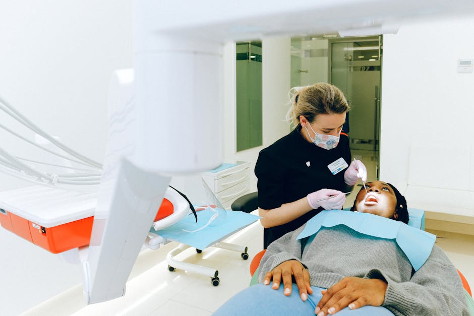 Concentrated female dentist in medical mask and gloves using metal medical instruments while healing teeth of female ethnic patient sitting in dental chair in modern clinic