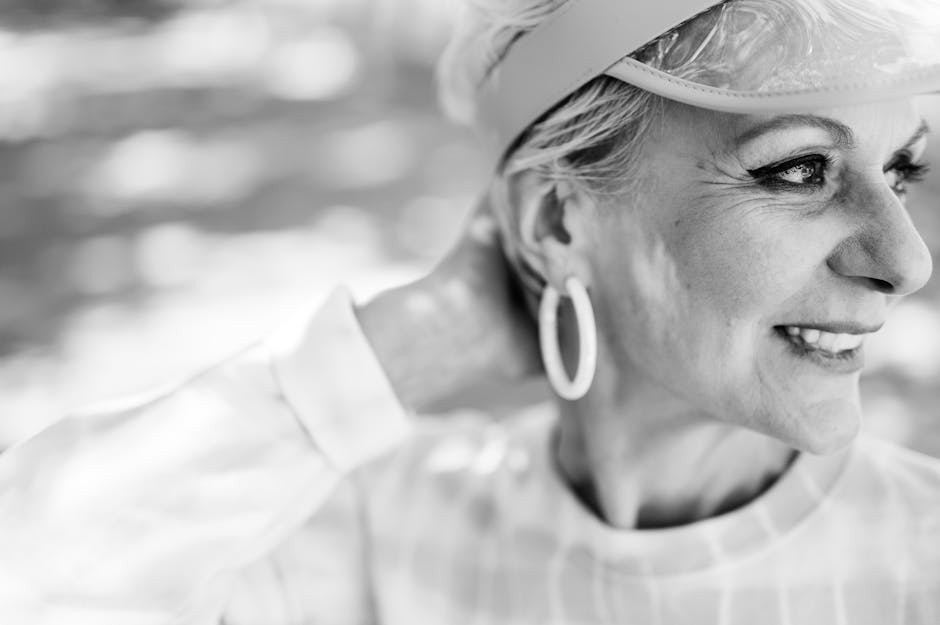 A smiling senior woman with an earring, captured in a classic black and white close-up portrait.