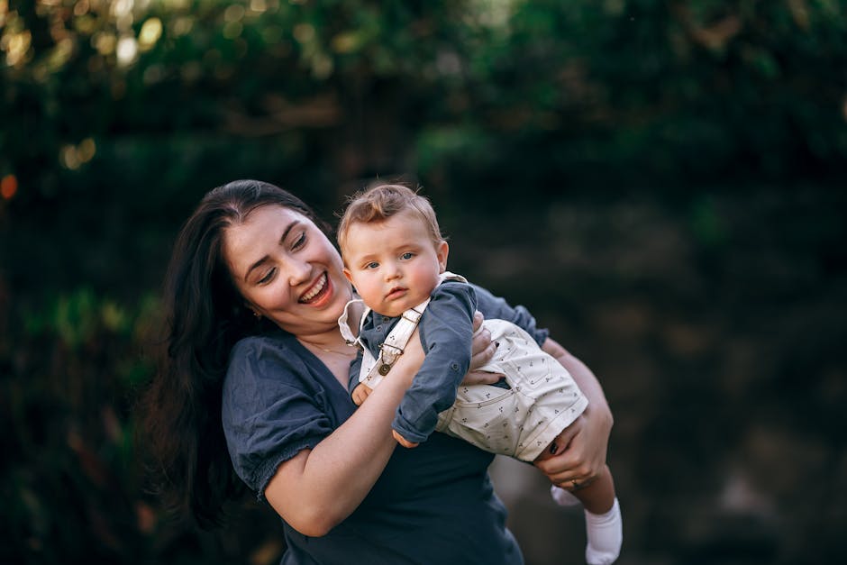 Smiling mother lovingly holding her baby in an outdoor setting with lush greenery.