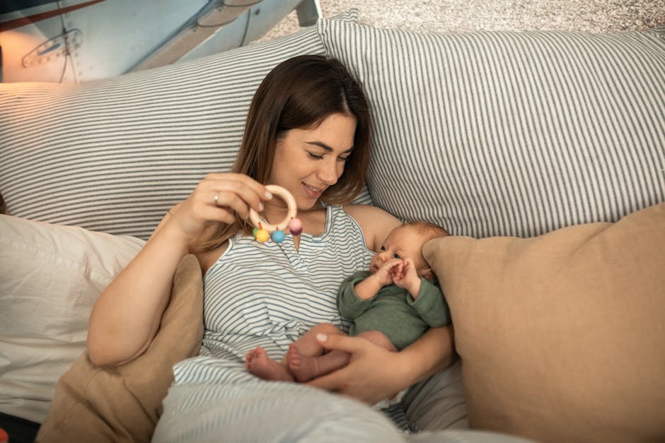 A mother joyfully playing with her newborn baby in a warm, cozy bedroom setting.