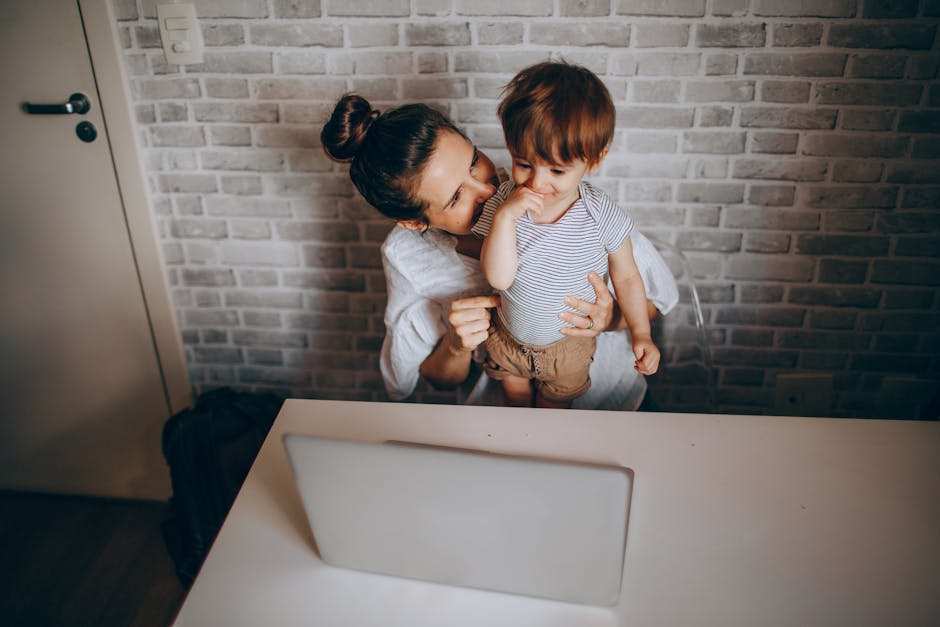 A mother lovingly interacts with her toddler while working on a laptop in a cozy home setting.