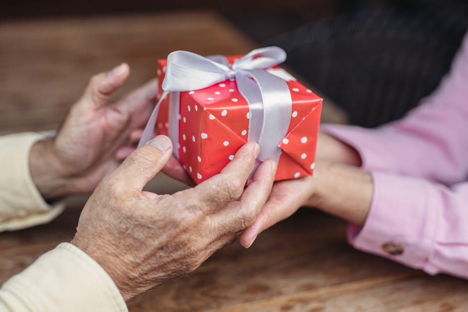 Close-up of senior hands exchanging a red gift box tied with a ribbon.