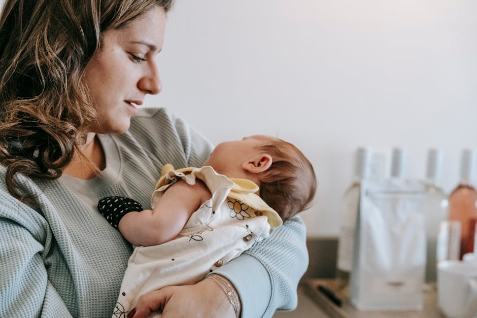 Side view of crop caring mother in casual wear with cute newborn baby in arms standing in light room at home