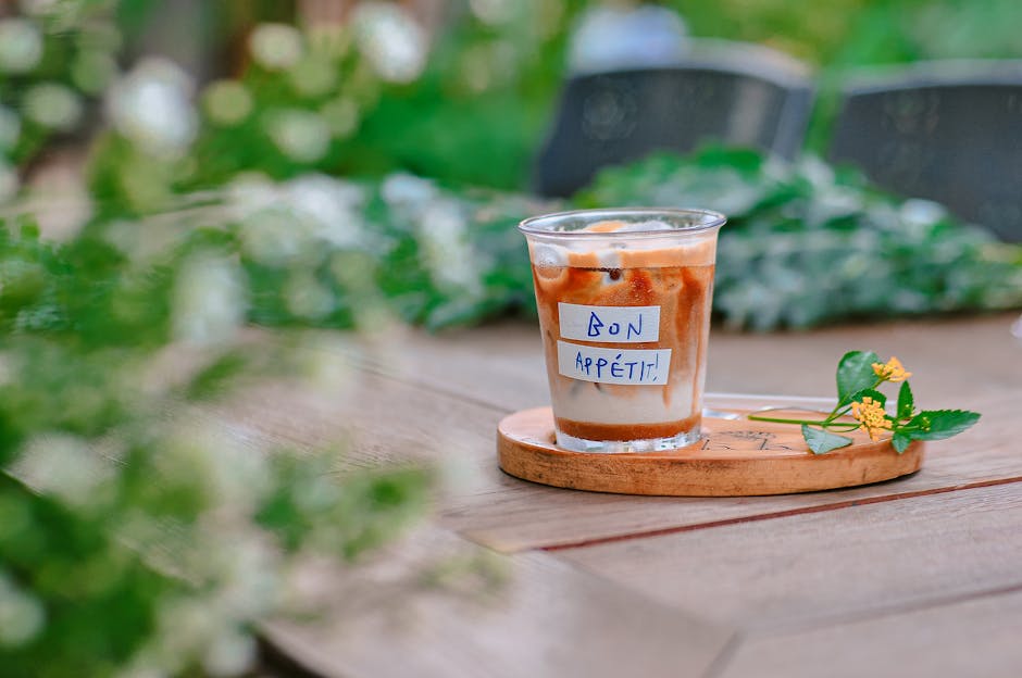Close-up of an iced coffee with a 'Bon Appétit' note on a wooden table outdoors.