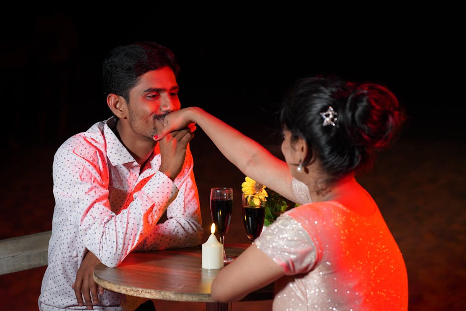 A couple enjoying a romantic candlelit dinner with wine and flowers on the beach.