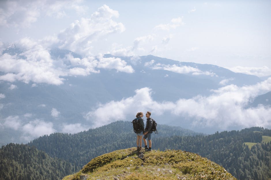 A couple with backpacks enjoys a scenic view from a mountain peak surrounded by clouds.