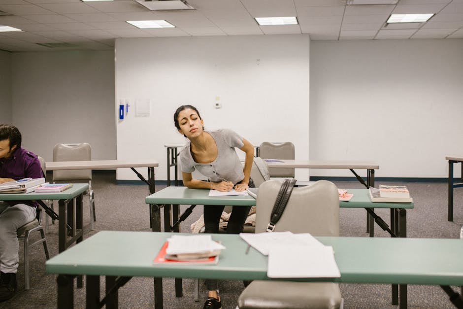 A college student appears to be cheating during an exam in a classroom setting, bending over to glance at another student's paper.