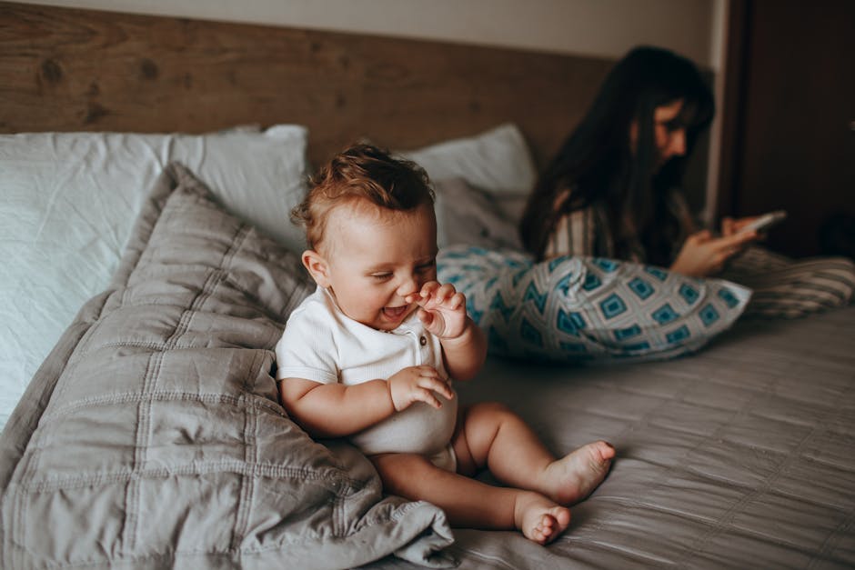 Adorable baby plays happily on a cozy bed while mother relaxes nearby, creating a warm family moment.
