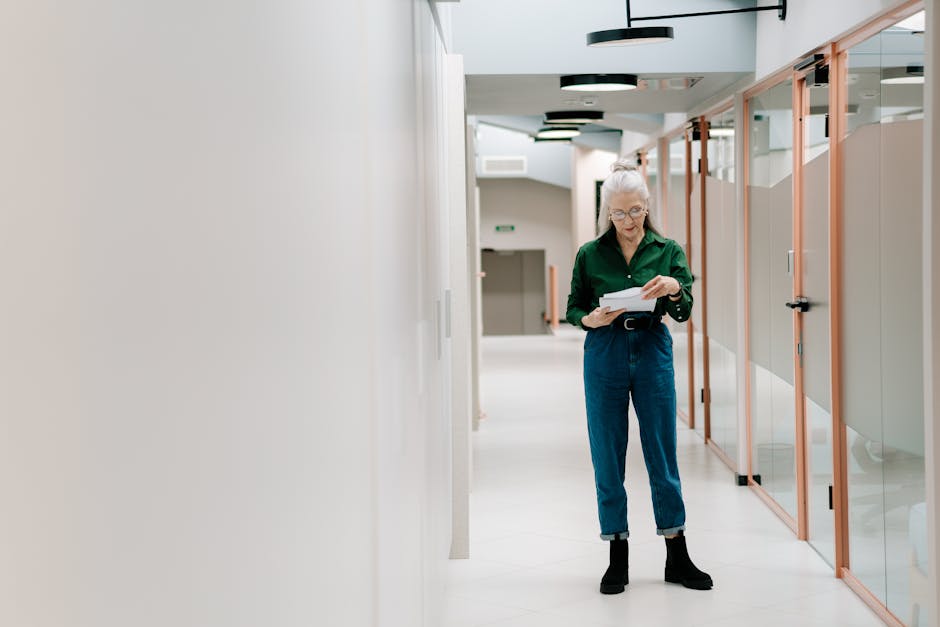 Elderly woman reviews documents in a contemporary office hallway, conveying professionalism and focus.