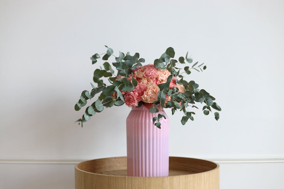 Beautiful floral arrangement with pink carnations and eucalyptus in a pink vase on wood table.