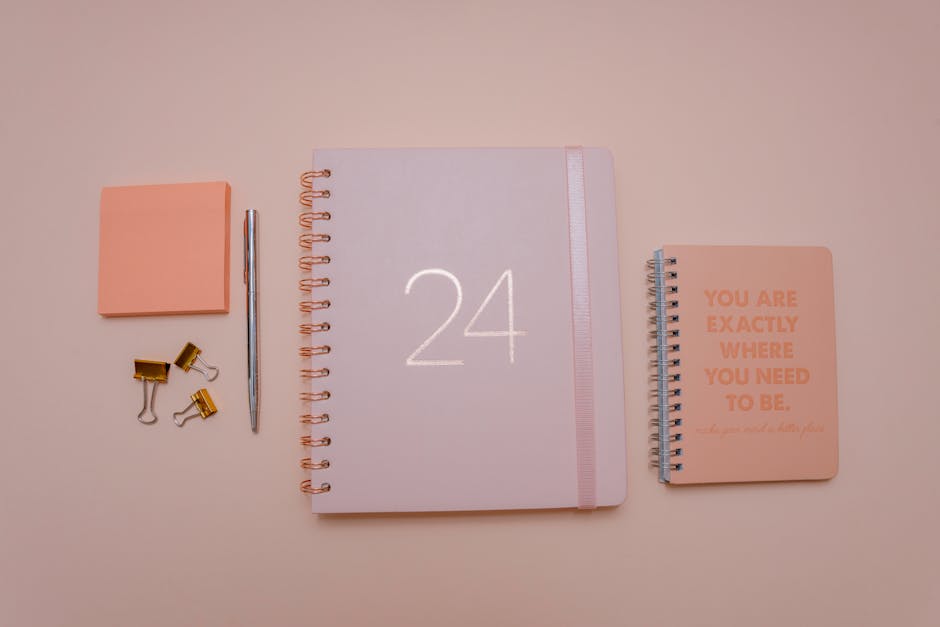 Peach-toned flat lay of office stationery including notebooks, pen, and clips for organized workspaces.