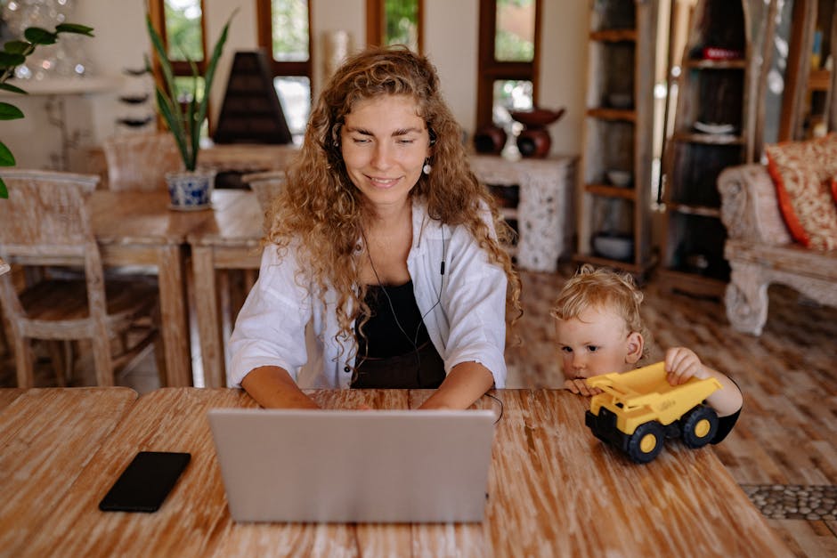 A woman working on a laptop at home with her child playing beside her, creating a balanced family lifestyle.