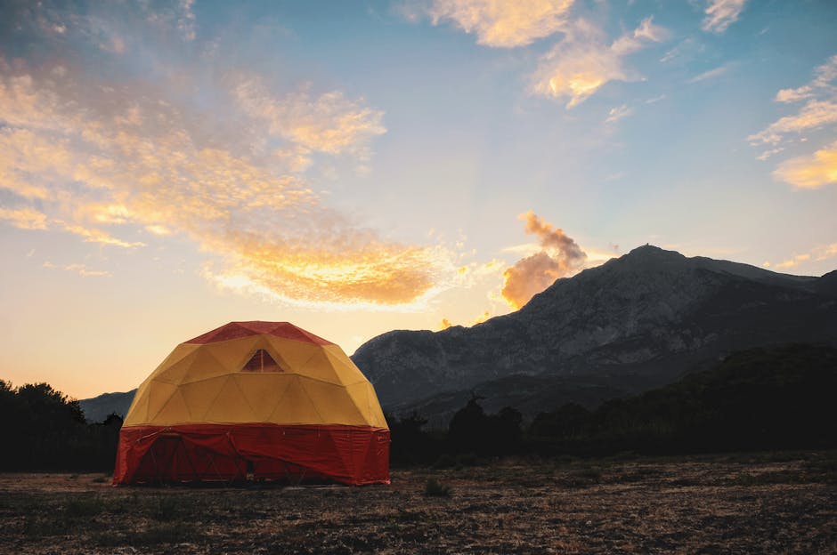 Geodesic tent under a vibrant sunset with mountains in the background.