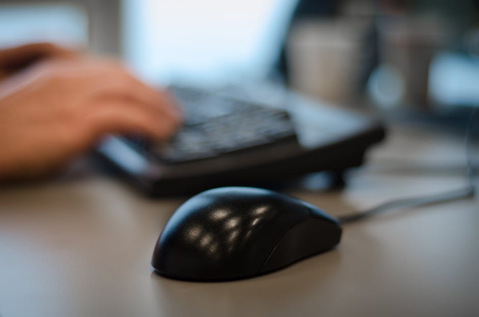 Blurry background with a focus on a computer mouse in an office setting.