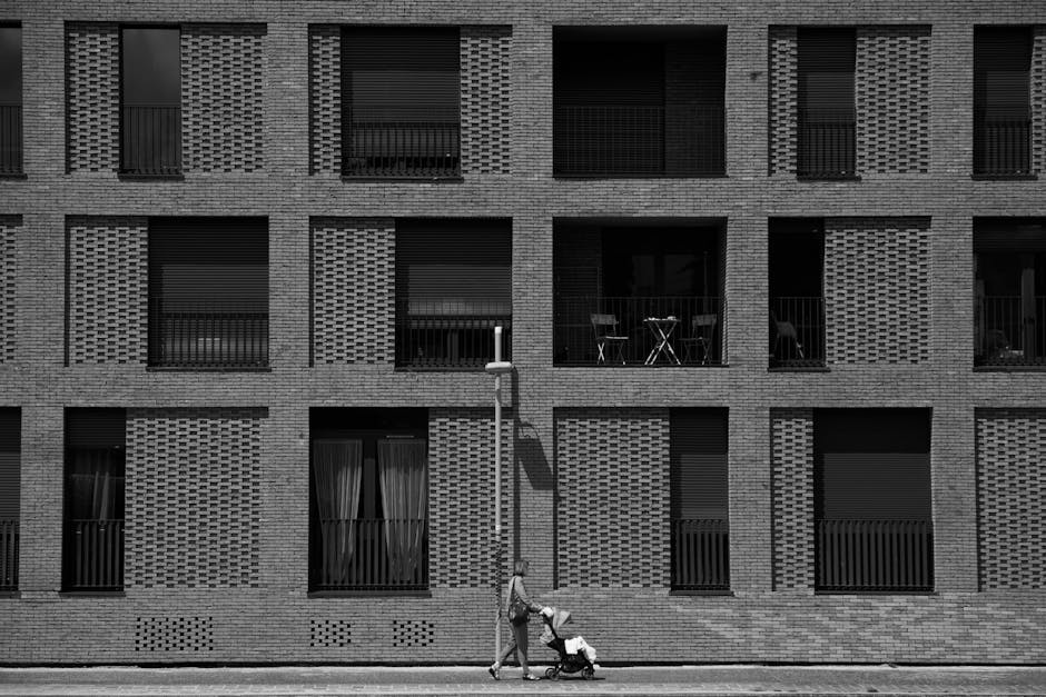 A woman pushing a stroller past a modern building facade in Paris.