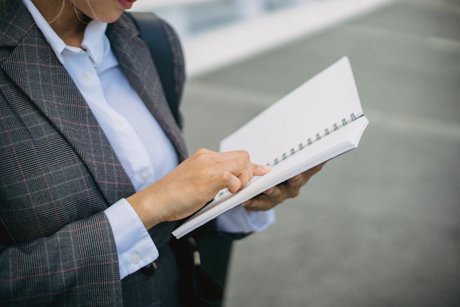 Close-up of a professional woman in a blazer writing in a notebook outdoors.