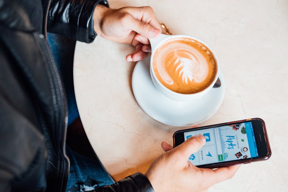 Close-up of person holding latte with beautiful latte art, browsing smartphone.