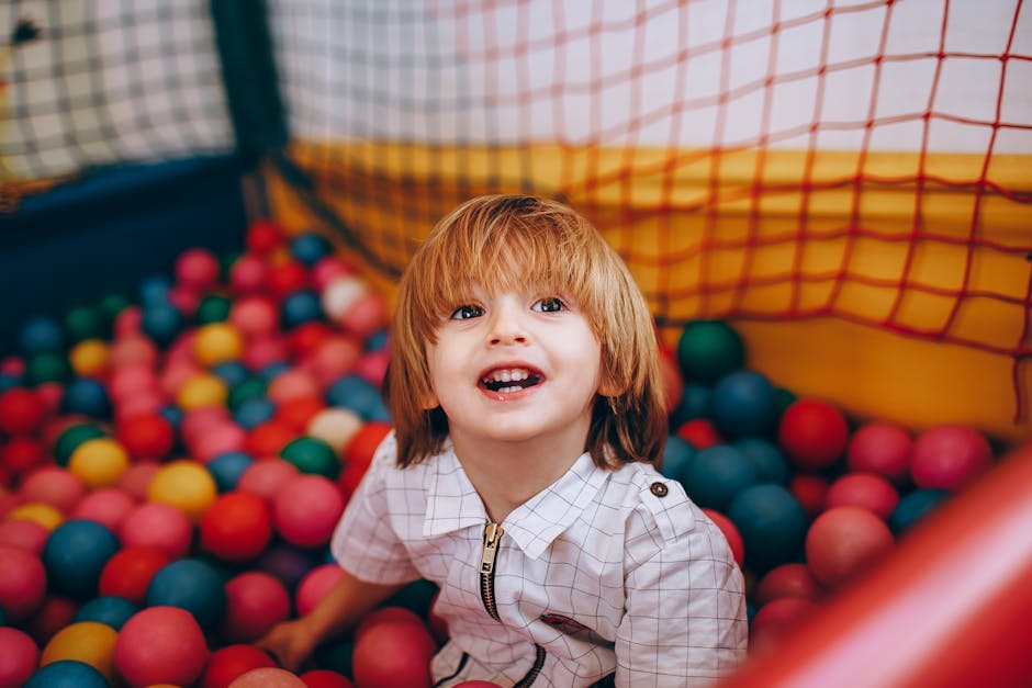 A joyful child sitting in a colorful ball pit indoors, expressing delight and fun.