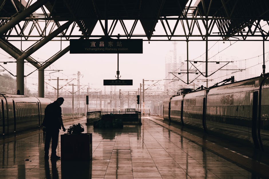 A silhouette of a man standing at Yichangdong Railway Station with trains and a rainy urban backdrop.