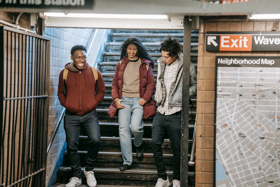 Full body of positive multiracial group of friends in warm clothes walking down staircase of subway station while entering metro