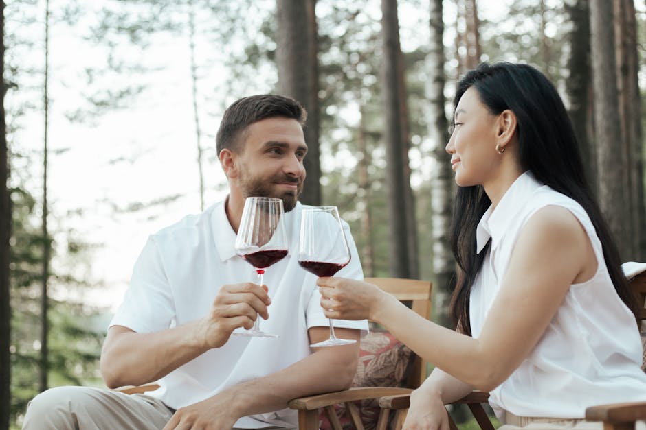 A couple clinks wine glasses while enjoying a serene moment in a forest setting.