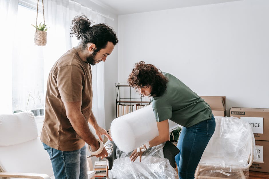 A couple wraps furniture with bubble wrap in a bright and modern apartment while preparing to move.