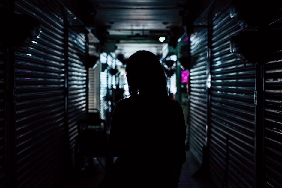 A silhouette of a person in a backlit dark urban alley, creating a mysterious atmosphere.