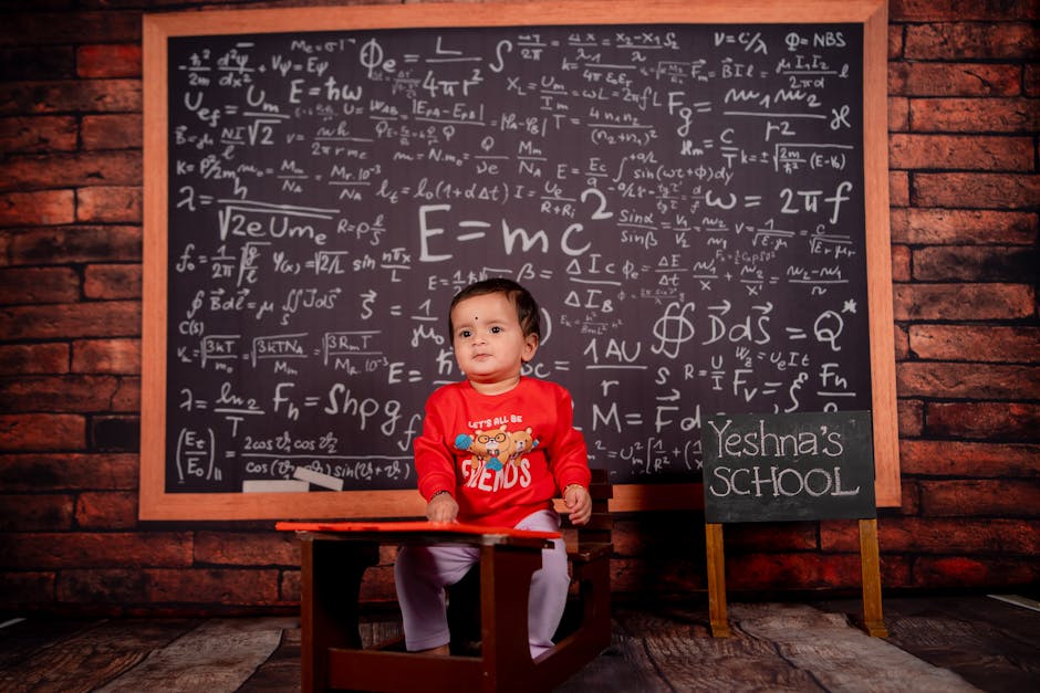 A baby in a classroom setting with a math-filled chalkboard background.