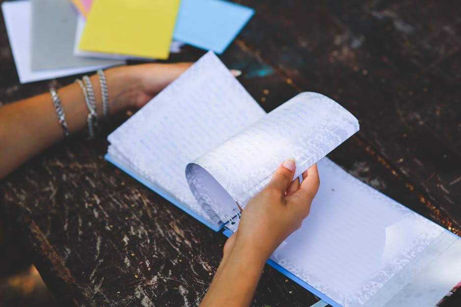 Close-up of hands flipping through a notebook on a worn wooden table. Outdoors setting, relaxed atmosphere.