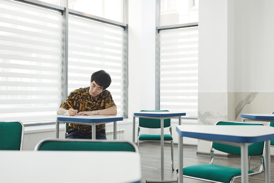 Young man taking notes in a bright, empty classroom with modern furniture.