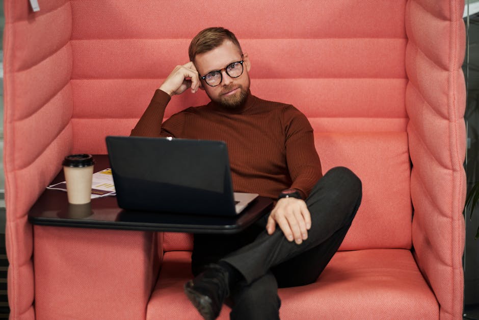 Man working in a cozy office booth with laptop and coffee, showcasing a modern workspace setup.