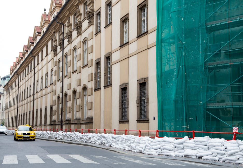 Street view with historical architecture, sandbags, and scaffolding on an overcast day.