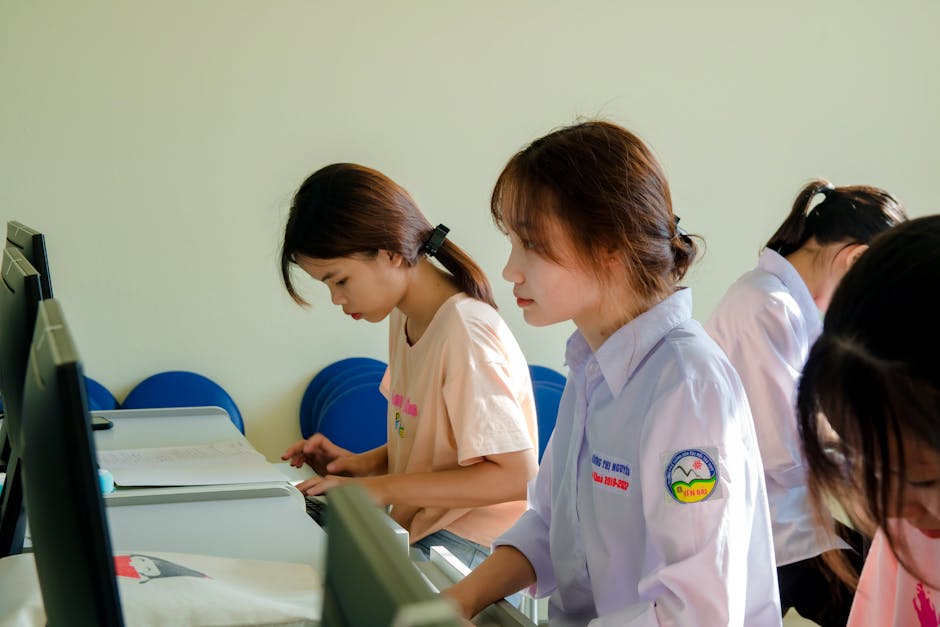 Three young women concentrating on a computer task in a classroom setting.