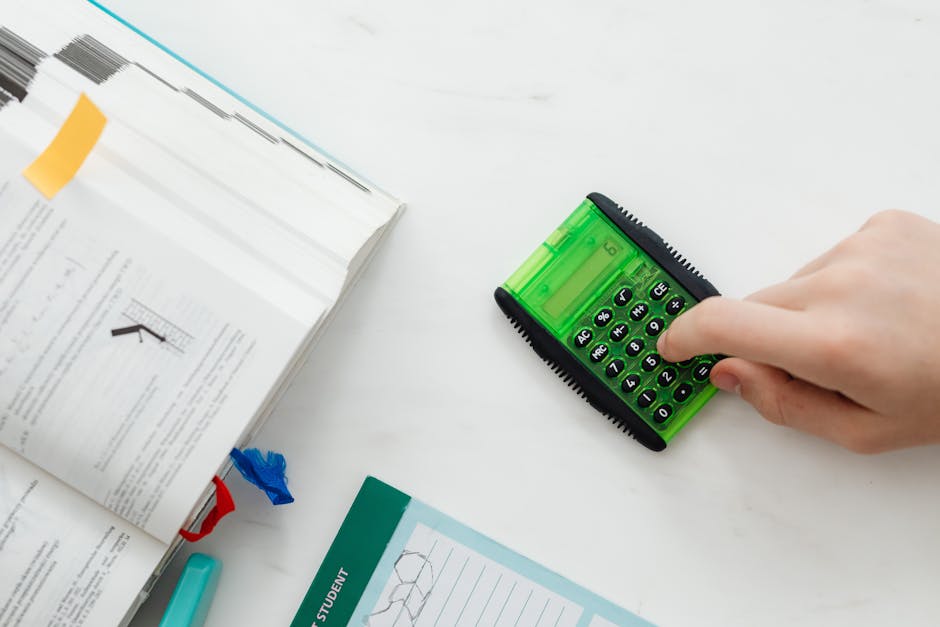 A student uses a green calculator to solve math equations from a textbook on a desk.