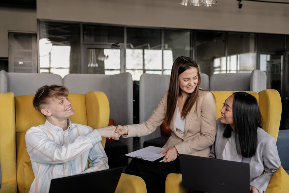 Three coworkers in a modern office shaking hands and collaborating on a project.