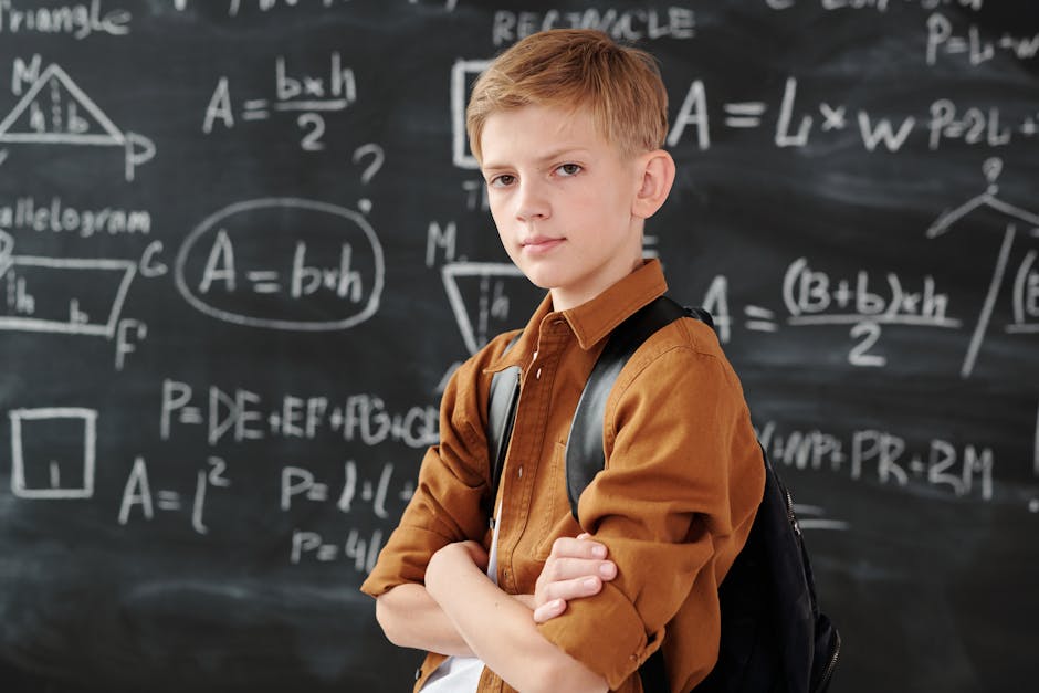 Young boy stands confidently with arms crossed in a classroom, in front of a blackboard covered with math equations.