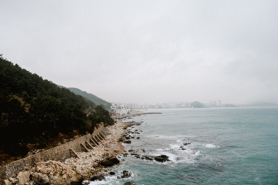 Scenic view of a rocky coastline leading to a distant city under cloudy skies.