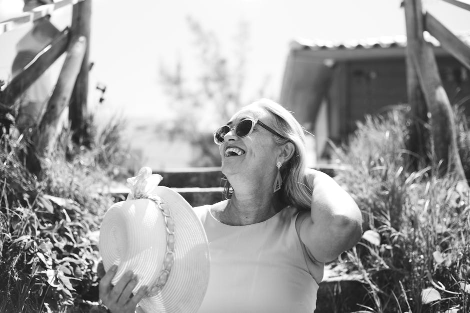 A smiling senior woman enjoys a sunny day outdoors wearing sunglasses and a sunhat.