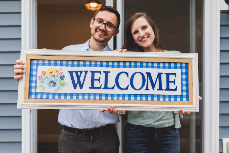 A smiling couple holds a cheerful welcome sign, expressing hospitality and warmth.