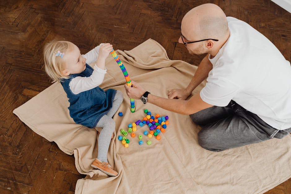 Father and young daughter bonding over a playful activity with colorful blocks on a wooden floor.
