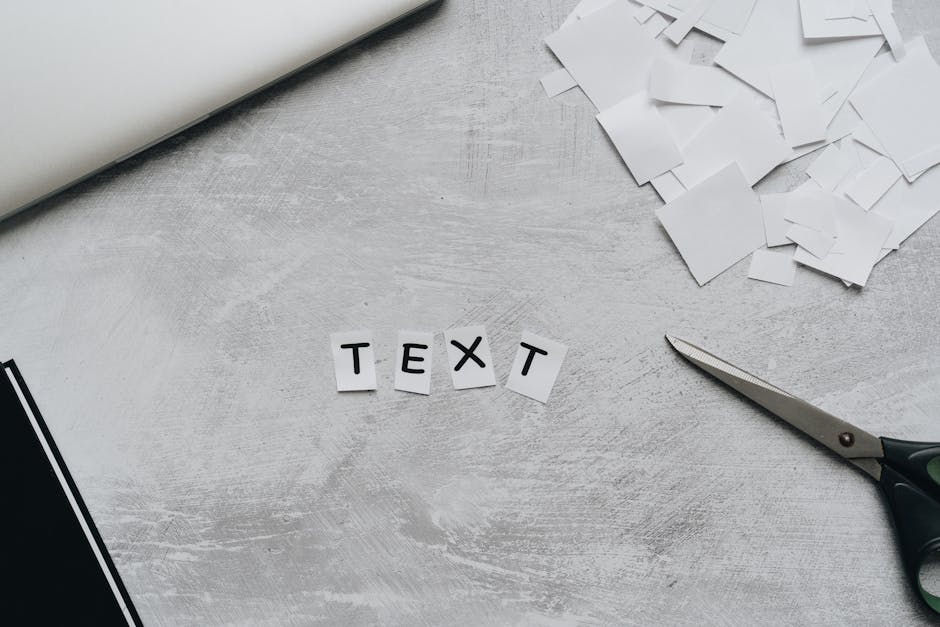 A flat lay of a creative workspace featuring cutout text, scissors, and paper pieces on a textured surface.