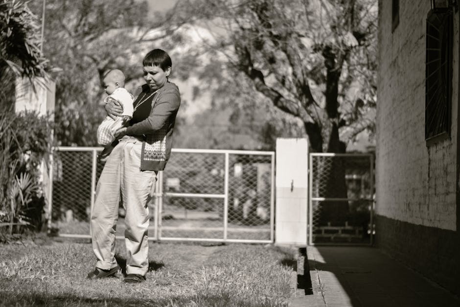 A mother holding her baby in a sunny rural setting, captured in black and white.