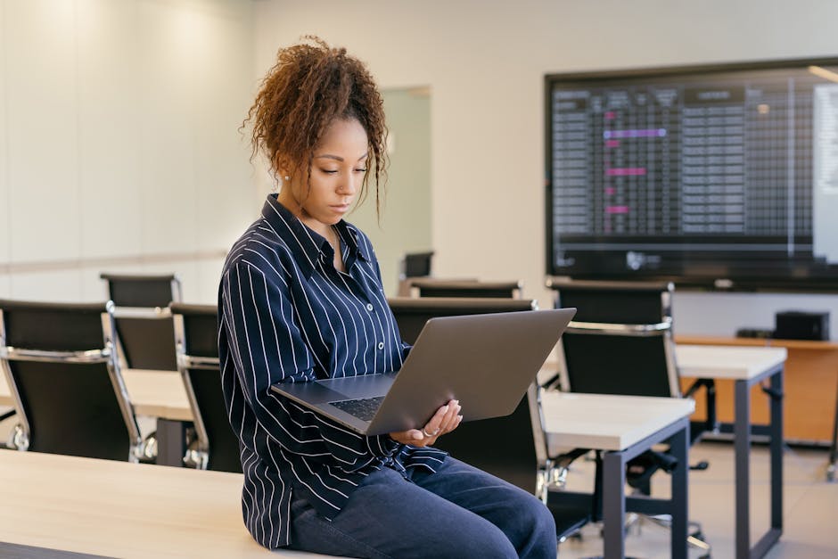 African American woman with curly hair working on a laptop in a modern office setting.